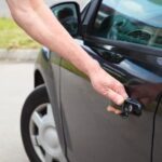 Man trying to open his car door but can't because he is locked out
