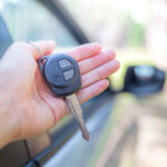 car key in woman's hand next to car with car besides