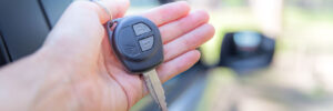 car key in woman's hand next to car with car besides