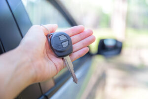car key in woman's hand next to car with car besides